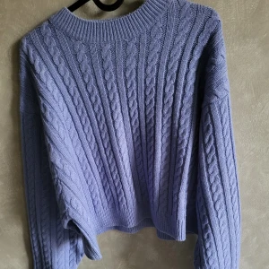 Ljuslila stickad tröja från Sinsay - Säljer en mysig ljuslila stickad tröja från Sinsay. Tröjan har ett klassiskt flätmönster och långa ärmar, perfekt för kyliga dagar. Den har en rund halsringning och ribbade kanter.