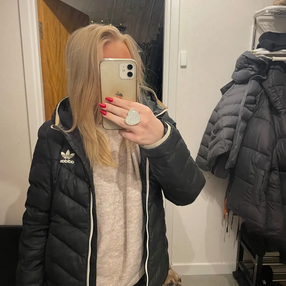 Säljer en svart dunjacka från Adidas med dragkedja och huva. Jackan har en sportig look med det klassiska Adidas-loggan.. Takit.