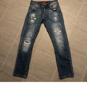 Vintage jeans från jacknjones  - Snygga blå jeans med slitningar på knäna och låren. De har en klassisk femficksdesign och en knappgylf. Perfekta för en avslappnad stil.