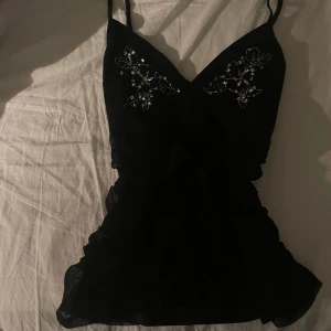Vintage 00s svart linne med paljettdetaljer - Supersnyggt svart linne med smala axelband och v-ringning. Toppen har vackra paljettdetaljer framtill som ger en glittrig effekt. .
