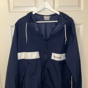 Mörkblå vindjacka från Columbia - Mörkblå vindjacka från Columbia som knappats används. Jackan är i 10/10 skick och har inga defekter. 