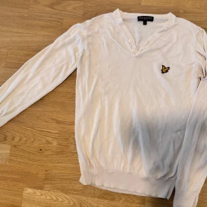 Vit tröja från Lyle & Scott - Säljer en stilren vit tröja från Lyle & Scott med en broderad logotyp på bröstet. Tröjan har en v-ringad design med knappar och långa ärmar. Perfekt för en avslappnad look. I mycket gott skick.