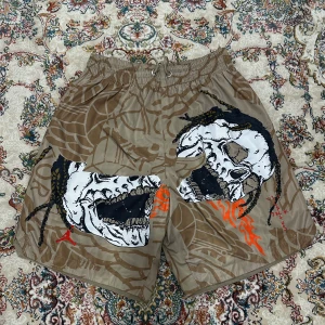 Travis scott badshorts  - Coola beige shorts från Jordan med ett unikt dödskallemotiv i svart och vitt, samt orange detaljer. Shortsen har en elastisk midja med snörning för bästa passform.