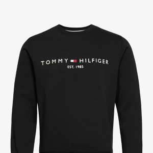 Svart sweatshirt från Tommy Hilfiger - Snygg svart sweatshirt från Tommy Hilfiger med deras ikoniska logga och texten 'Est. 1985' på bröstet. Ny. pris 1300kr