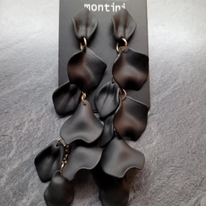 Svarta örhängen från Ur&penn  - Eleganta svarta örhängen från Montini med unika, böljande former som ger en modern och stilren look. Perfekta för att lyfta vilken outfit som helst med en touch av sofistikation.