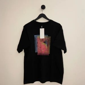Maison Margiela T-shirt - Snygg svart t-shirt från Maison Margiela med ett unikt, färgglatt tryck i rosa, gult och blått på framsidan. Perfekt för dig som vill sticka ut med stil. T-shirten har en klassisk passform och är kortärmad. Den är endast testad med tags på! Hör gärna av er vid flera frågor eller funderingar!🌟💯