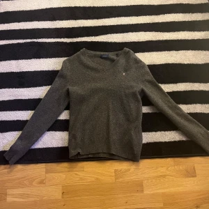 Grå ulltröja från Gant - Säljer en stilren grå ulltröja från Gant med v-ringning. Tröjan har långa ärmar och en liten broderad logotyp på bröstet. Perfekt för kyligare dagar. Storlek M 