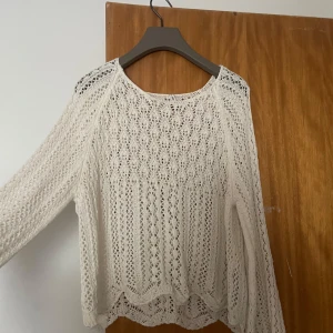 Vit stickad tröja - Säljer en vit stickad tröja med ett vackert spetsmönster. Tröjan har långa ärmar och en rund halsringning. Passar bra till både jeans och kjol.