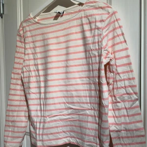 Randig långärmad tröja från & Other Stories - Säljer en söt randig tröja från & Other Stories i vitt och rosa. Tröjan har långa ärmar och är perfekt för en avslappnad stil. Tillverkad i ett mjukt material som känns skönt mot huden. Passar perfekt till jeans eller kjol för en casual look.