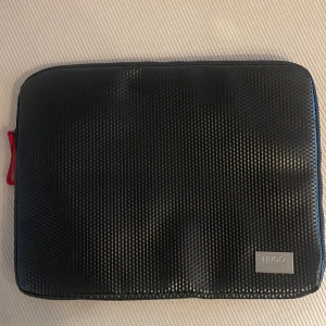 Svart datorväska från Hugo Boss - Snygg och stilren svart datorväska från Hugo Boss med ett coolt mönster. Perfekt för att skydda din laptop med stil. Väskan har en diskret logotyp och en praktisk dragkedja.