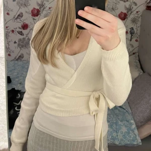 Vit omlottkofta - Säljer en stilren vit omlottkofta med knytband i midjan. Koftan har långa ärmar. Passar bra till både vardag och mer uppklädda tillfällen.