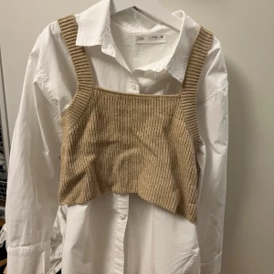 Vit skjorta och Beige stickad väst från Zara  - Säljer en vit skjorta med beige stickad väst från Zara. Den har breda axelband och en ribbad design som ger en snygg look. Skjortan går att använda utan väst