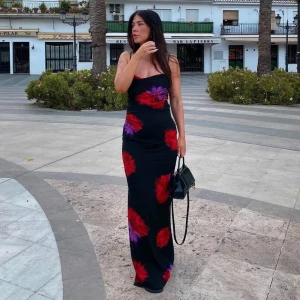 Adoore klänning - Storleken på lappen är 32 men passar även 34! Svart långklänning med röda och lila blommor från adoore. Klänningen har smala axelband och en öppen rygg med snörning. Perfekt för bal, middag eller en utomlandskväll😍🤩 