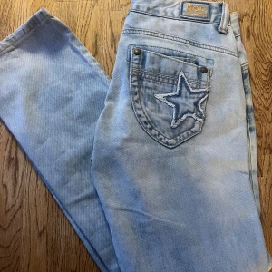 Ljusblå jeans med stjärndetalj från Mod Jeans - Storlek w27 L32, upplevs rätt så små. Snygga ljusblå jeans från Mod Jeans med en cool stjärndetalj på bakfickan. De har en klassisk femficksdesign och knappgylf. Perfekta för en avslappnad stil med en unik touch.