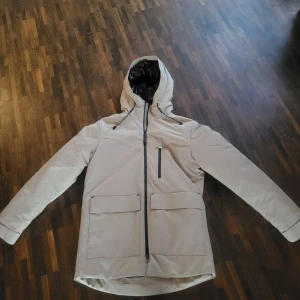 Beige parkajacka från Jack & Jones (Aldrig använd) - Säljer en stilren beige parkajacka från Jack & Jones. Jackan har en dragkedja framtill och praktiska fickor. Perfekt för kyligare dagar med sin långa ärm och skyddande huva. En snygg och funktionell jacka för alla tillfällen.