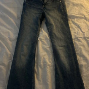 Blå jeans från Divided - Snygga blå jeans från Divided med klassisk femficksdesign och knappgylf. De har en bootcut-stil som ger en retro vibe. Perfekta för en avslappnad look.