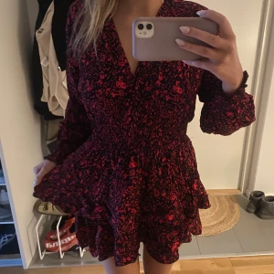 Röd och svart klänning med volang - Snygg sommrig klänning med blommigt mönster och volang. Klänningen har långa ärmar och med markerad midja. Använt fåtal gånger och den är i bra skick!! 💓