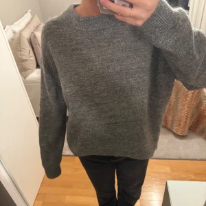 Grå stickad tröja - Säljer en mysig grå stickad tröja med långa ärmar och lite glittrig. Perfekt för kyliga dagar och enkel att matcha med olika outfits. Tröjan har en klassisk design och är bekväm att bära🤍