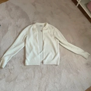 Vit kofta  - Säljer en elegant vit kofta från Orsay. Den har långa ärmar med pärldetaljer och en ribbad krage. Den är i storlek S och är knappt använd 
