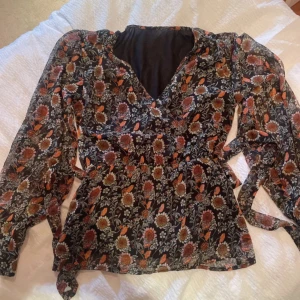 Blommig blus med volangdetaljer - Säljer en superfin blommig blus med volangdetaljer. Den har en v-ringad design och långa ärmar. Perfekt för både vardag och fest! 🌸Samt så går det och knyta till midjan☺️