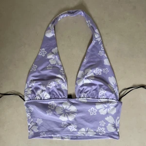 Lila blommig bikiniöverdel - Säljer en superfin lila topp med vita blommor. Den har en halterneck-design för perfekt passform. Perfekt för sommarens alla stranddagar! 🌸