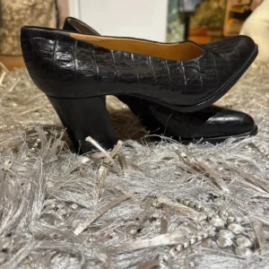 Svarta pumps med krokodilmönster - Säljer ett par eleganta svarta pumps med ett coolt krokodilmönster. Skorna är lite stora i storleken är 36 men passar ej mig som bara har 36