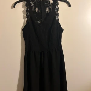 Svart kort spets klänning - En svart kort spetsklänning med volang nedtill och spets vid bysten och ryggen. Oanvänd