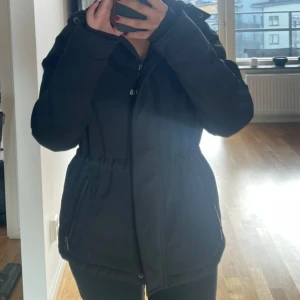 Svart parkajacka med huva - Säljer en svart varm parkajacka som är perfekt för kyliga dagar. Jackan har en dragkedja framtill och långa ärmar. Den är i bra skick och passar perfekt för höst och vinter. 