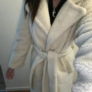 Teddy kappa - I fint skick förutom ett hål i ena fickan och att 2 knappar fattas men det är inget man lägger märket till när man använder kappan då det finns ett bälte som man stänger kappan med. Creamefärgad 