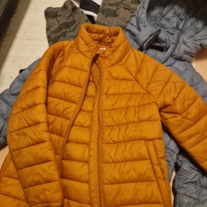Orange och blå jacka från Everest - Säljer två jackor från Everest. Den ena är en orange quiltad jacka i storlek 116, perfekt för höst och vår. Den andra är en blå jacka med orange detaljer och dragkedjor i storlek 122, idealisk för vinter. Båda jackorna är i bra skick och redo för nya äventyr!