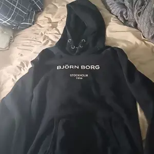 Säljer en svart hoodie från Björn Borg med texten 'STOCKHOLM 1956' på bröstet. Den är supermjuk och perfekt för kyliga dagar. Har en stor ficka fram och en justerbar huva. Perfekt för både vardag och chill! 🖤