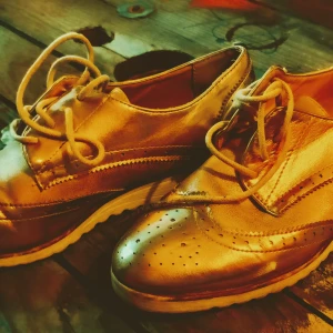 Guldiga brogues i skinn - Säljer ett par snygga guldiga brogues i skinn. De har klassiska broguemönster och snörning framtill. Perfekta för att ge en touch av stil till vilken outfit som helst!