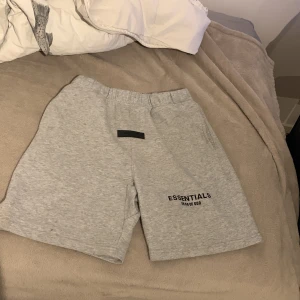 Grå shorts från Fear of God Essentials - Snygga grå shorts från Fear of God Essentials med elastisk midja och logga tryckt framtill. Perfekta för en avslappnad och trendig stil. Tillverkade i mjuk bomull för maximal komfort.