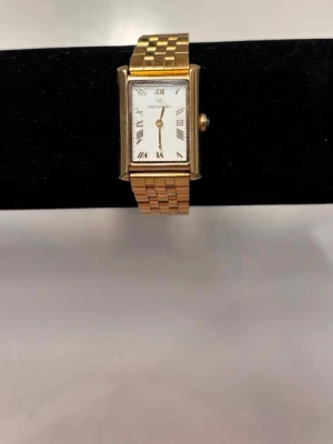 Mockberg klocka - Elegant guldfärgad klocka från Mockberg. Klockan har en stilren rektangulär urtavla med romerska siffror och ett klassiskt guldfärgat armband som passar både till vardag och fest.    Den är i fint skick och ger en väldigt lyxig och tidlös känsla. Perfekt accessoar om du vill ha en minimalistisk men elegant look.    Batteriet behöver bytas. Missfärgningar på lister, men syns knappt (kan skickar bilder)!  ✨ Märke: Mockberg   ✨ Färg: Guld   ✨ Modell: Rektangulär urtavla med romerska siffror  