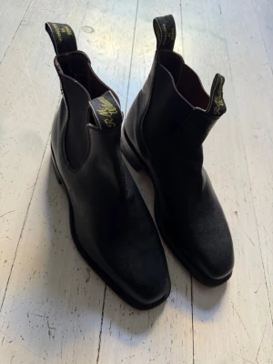 R.M Williams boots - Säljer ett par klassiska svarta Chelsea boots i äkta skinn med elastiska paneler på sidorna. Dessa har använts 3-4 gånger. Köpte det som en present till bruden, men dum som jag är kunde jag inte hennes storlek. Det blev lika med missnöjd brud och pengar i sjön… Storlek 5/12g vilket är 38,5-39 EU