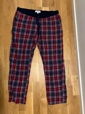 Rödrutiga pyjamasbyxor med resår💙❤️🖤 - Snygga pyjamasbyxor i röd, blå och vit rutigt mönster. Byxorna har svart resår i midjan med dragsko för skön passform. Perfekta för mysiga hemmakvällar och avkoppling. Tillverkade i mjukt tyg som känns bekvämt mot huden.