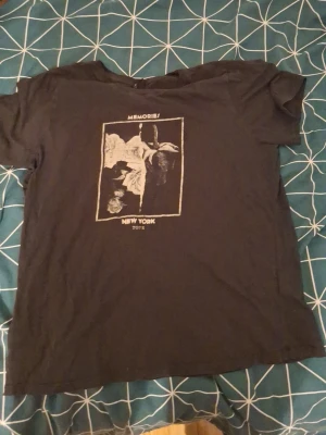 Svart t-shirt från Gina Tricot XL - Svart t-shirt från Gina Tricot med tryck framtill där det står 'MEMORIES' och 'NEW YORK'. T-shirten har korta ärmar och en klassisk rund halsringning. Perfekt för en avslappnad och cool stil.