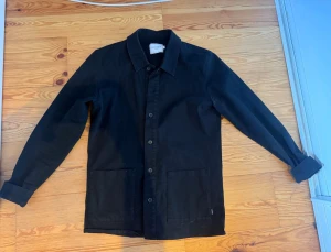 Svart overshirt - Stilren svart overshirt med knäppning framtill och två stora fyrkantiga fickor. Klassisk krage och långa ärmar som kan vikas upp. Tillverkad i ett kraftigare tyg som ger en schysst streetkänsla. Perfekt att slänga över en hoodie eller t-shirt.