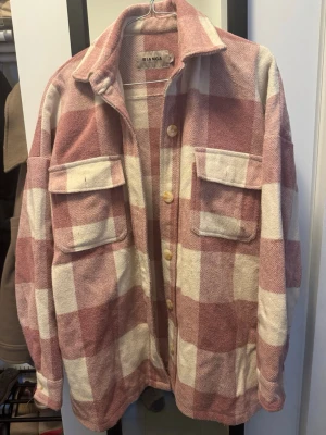 Rutig overshirt/oversized jacka från Bianca  - Oversized jacka i mjukt ”tweed” material från Bianca med stora rutor i rosa och vitt. Jackan har två bröstfickor med lock, klassisk krage och knäppning framtill med ljusa knappar. Perfekt för lager-på-lager och en chill look. Någon små noppra här och där men betydelselös, varsamt använd och jag tycker det är väldigt fint skick men alla tycker olika. Tycker den värmer långt in på hösten. 