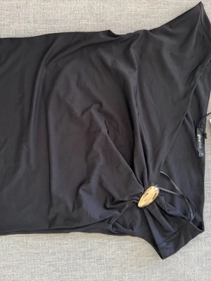 Svart metall detalj topp Gina Tricot - Snygg svart topp från Gina Tricot med en unik metall detalj på sidan. Toppen är ärmlös och har en cool drapering vid metallringen. Perfekt för dig som vill ha en stilren men ändå trendig look.