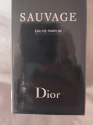 Dior Sauvage Eau de Parfum 100ml - Dior Sauvage Eau de Parfum är en lyxig herrdoft i en elegant mörkblå rektangulär flaska, förpackad i en stilren svart kartong med silverdetaljer. Flaskan rymmer 100 ml och utstrålar exklusivitet och modern stil.