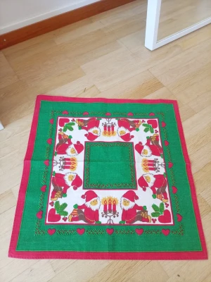 Julduk med tomtar och ljus - Julduk med motiv av tomtar, ljus och hjärtan. Duken har en grön mitt och en röd känt. Den ä 49X49cm