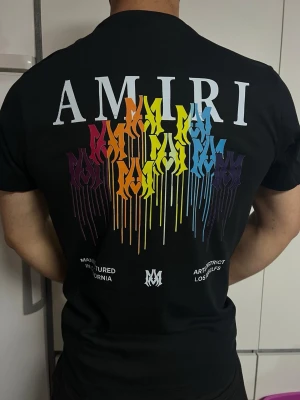 AMIRI svart T-shirt med färgglatt ryggtryck - Svart AMIRI T-shirt med stilrent tryck framtill och stort färgglatt motiv på ryggen. Snygg streetwear-design och bekväm passform. I mycket fint skick.