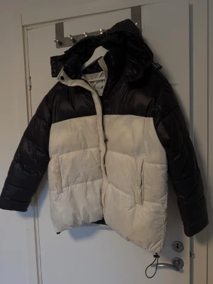 Svart och vit vinterjacka från NA-KD - Snygg och varm vinterjacka från NA-KD i storlek 36. Jackan är svart upptill och vit nedtill, har huva och dragkedja framtill. Perfekt för kalla vinterdagar! Köp direkt eller lägg ett bud.