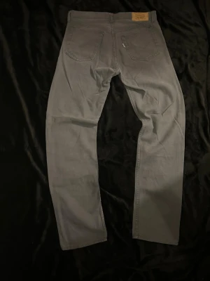 Levis jeans - Säljer ett par grå/blå jeans med raka ben och klassiska bakfickor. Jeansen har en enkel design utan slitningar eller dekorationer och är tillverkade i ett mjukt denimtyg. Perfekta för en clean och stilren look.