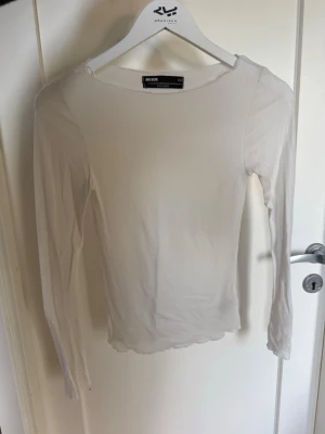 Vit långärmad topp från Bik Bok - En enkel och stilren vit långärmad topp från Bik Bok. Modellen är tight med rund halsringning och har vågiga kanter vid ärmslut och nederkant. Perfekt att matcha med jeans eller kjol för en clean look. Woolblend. Intimissimi liknande topp.