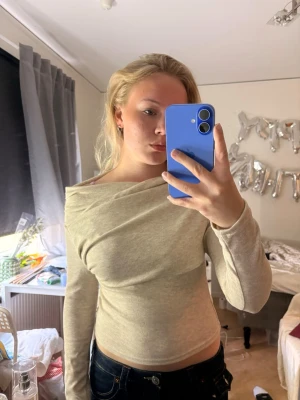Beige långärmad omlottopp - Trendig beige omlottopp med lång ärm och snygg offshoulder-design. Toppen har en mjuk och stretchig känsla, perfekt för att styla med jeans eller kjol. Materialet känns som bomull eller en bomullsblandning.