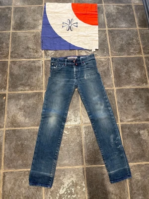 Blå smala jeans från Jacob Cohen - Dom är 134 långa helt nya Snygga blå jeans från Jacob Cohen med smal passform och klassisk femficksdesign. Jeansen har slitningar och ljusa tvättade partier för en trendig look. Röd detalj vid gylfen och kontrastsömmar ger extra stilpoäng. Perfekta för dig som gillar en modern och avslappnad stil.