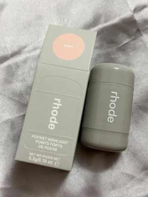 Rhode Pocket Highlight Pearl - Rhode Pocket Highlight i färgen Pearl är en krämig highlighter i stickformat. Förpackningen är stilren och grå med vit text. Perfekt att ha med i väskan för en snabb glow-up. Innehåller 5,3g produkt.