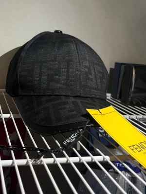 Fendi keps - Snygg svart keps från Fendi med det klassiska FF-logomönstret över hela kepsen. Böjd skärm med en stilren look och justerbar passform. Materialet ser ut att vara en mix av textil och läderdetaljer på skärmen. Perfekt för dig som gillar exklusiva accessoarer.